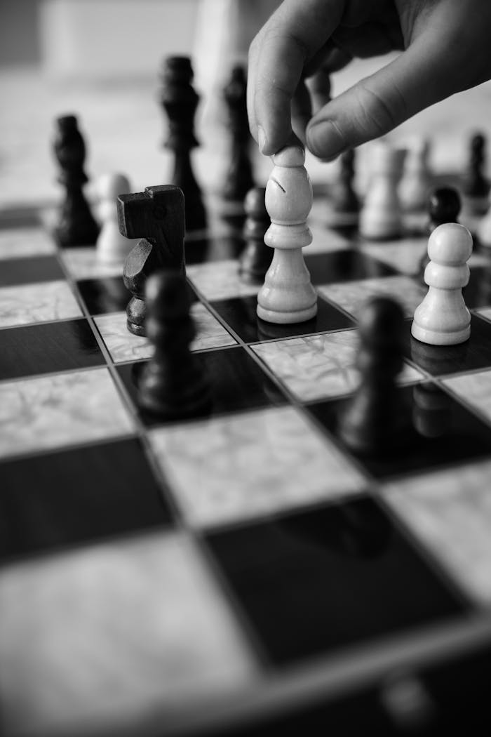 Black and white photo of a hand moving a chess piece on a chessboard.